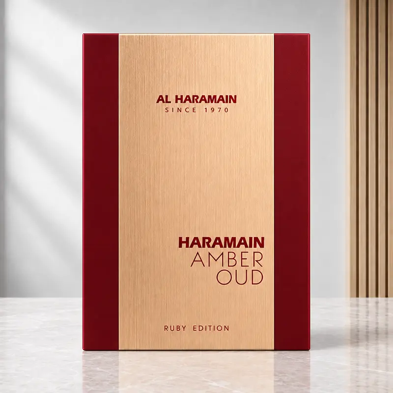 Front view of the Amber Oud Ruby Edition box with brushed-gold centre and ruby-red side panels.