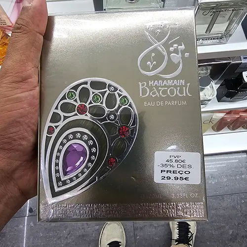 Batoul Eau de Parfum box held inside a perfume shop, showing its metallic finish, price sticker and jewelled design.