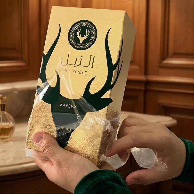 Close-up view showing hands actively removing the protective plastic cellophane shrink wrap from the textured gold box.