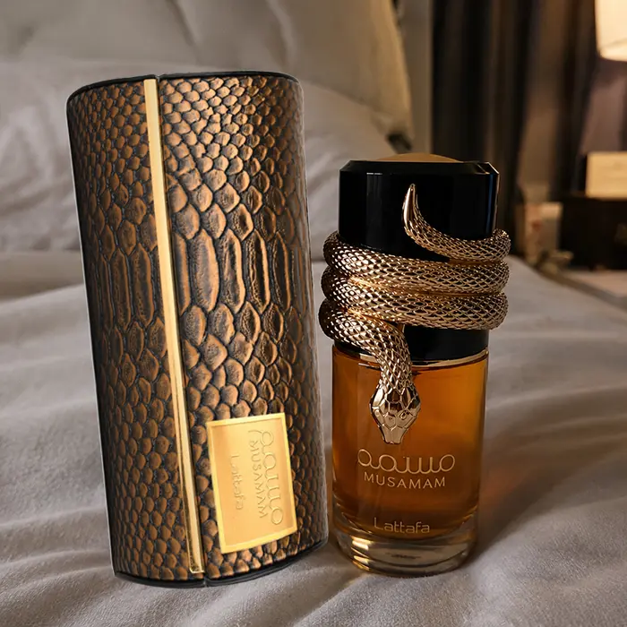 Warm lifestyle presentation featuring Musamam on soft bedding with its decorative fragrance case.