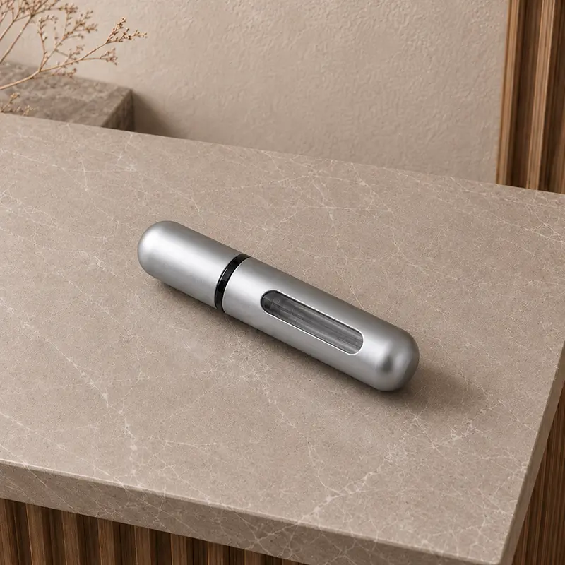 Silver refillable travel perfume atomizer with clear side window on a stone surface