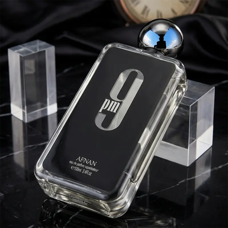 Reflective glass and metallic cap detail of Afnan 9 PM parfum bottle in a luxury presentation.